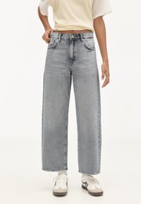 Jeans a gamba larga e vita alta in denim grigio chiaro con una finitura sbiadita. Presentano tasche anteriori e una chiusura con zip. Abbinate a sneakers bianche.