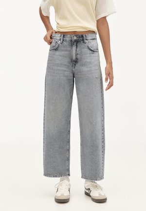 Široké, vysoko pasové džíny z světlého šedého denim s vybledlým vzhledem. Obsahují přední kapsy a zip. V kombinaci s bílými teniskami.