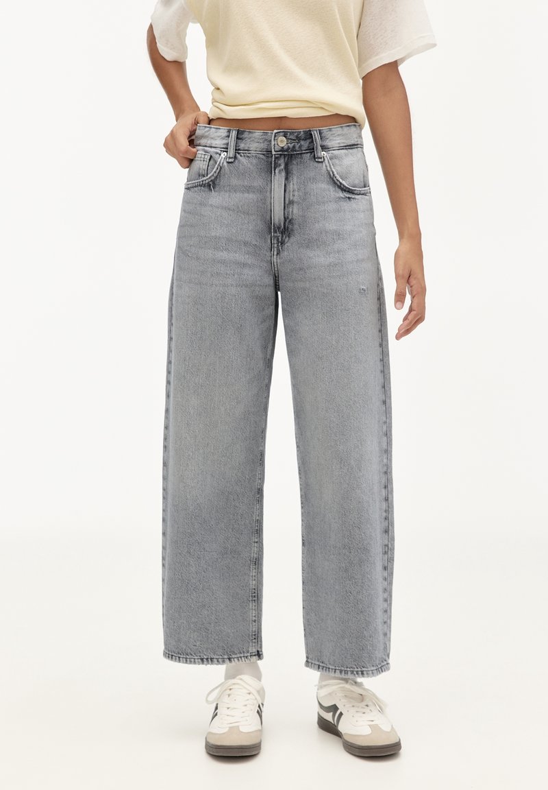 Jeans a gamba larga e vita alta in denim grigio chiaro con una finitura sbiadita. Presentano tasche anteriori e una chiusura con zip. Abbinate a sneakers bianche.