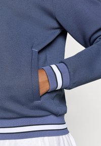 Blauwe sweatshirt met ribbelmanchetten en -zoom. Heeft horizontale streepaccenten in wit en zwart, gestructureerde stof en een zijzak.