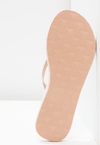 Talpă de sandale de cauciuc de culoare tan, cu un model texturat care prezintă forme mici de inimă, evidențiind o suprafață netedă și o formă rotundă.