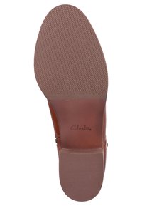 Hnědá podrážka z kůže s texturovaným gripem, má kulatý tvar a vyražený název značky "Clarks" blízko paty.