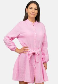 Abito button-down rosa con tessuto testurizzato, maniche lunghe, cintura a fiocco in vita e colletto arrotondato, caratterizzato da una gonna leggermente svasata.