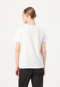 T-shirt bianco in cotone con maniche corte, scollatura arrotondata e vestibilità comoda, indossato con pantaloni in denim scuro. Vista posteriore mostrata.