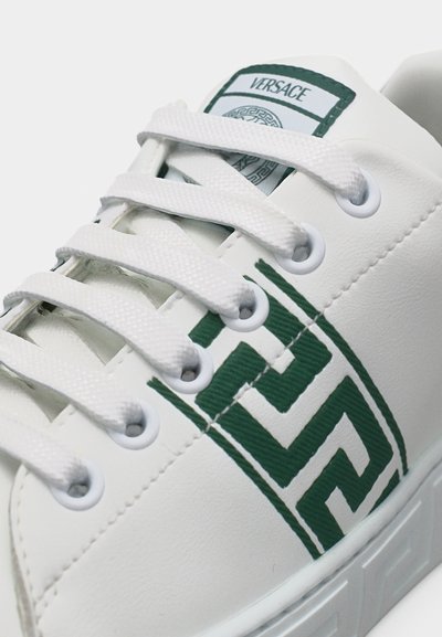 Baskets blanches avec des lacets blancs, un motif géométrique vert sur le côté et un patch avec le logo Versace sur la languette.