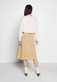 Beige cotton skirt with a flared design, knee-length, paired with a light-colored loose-fitting top and white ankle boots.