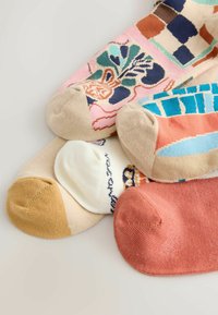 Štyri páry ponožiek v rôznych farbách: ružová, béžová, biela a koralová, s kvetinovými a geometrickými vzormi a kontrastnými koncami prstov.