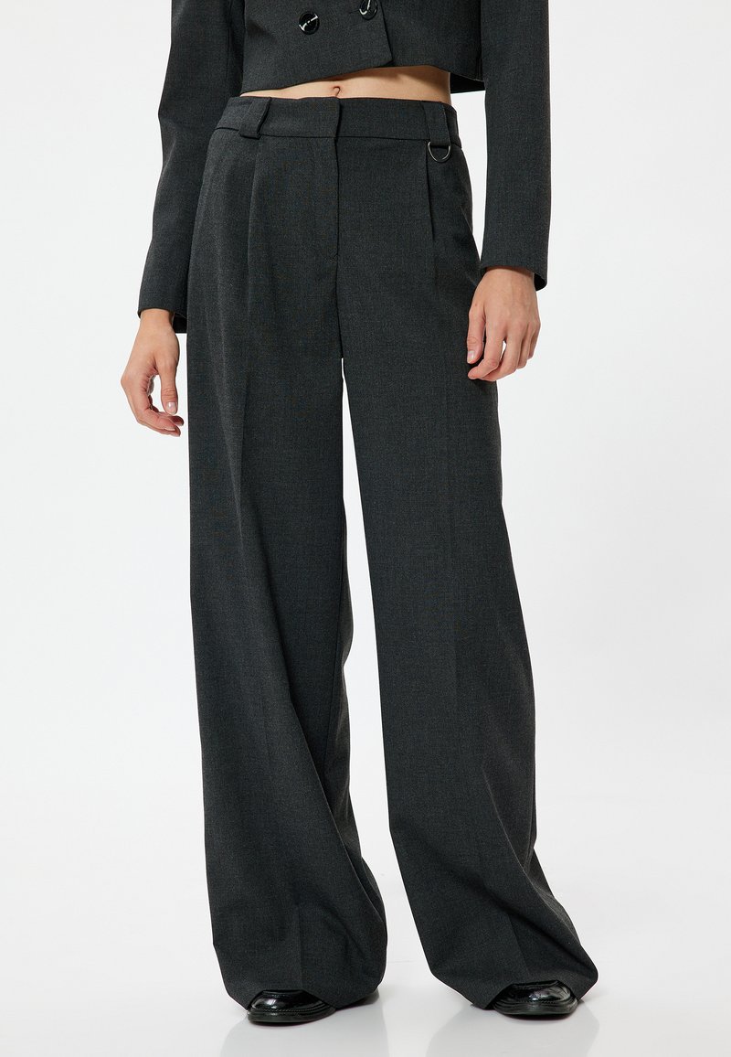 Pantalons larges gris avec un tissu texturé, présentant une taille haute, des poches latérales et des passants de ceinture. Fini lisse et plis subtils.