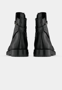 Bottines noires en cuir avec des languettes de tirage et des boucles latérales, présentées de dos sur un fond blanc uni.