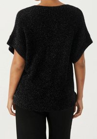 Pull noir à manches courtes avec une finition texturée et scintillante. Coupe ample avec un ourlet arrondi, fabriqué en matériau doux et léger.