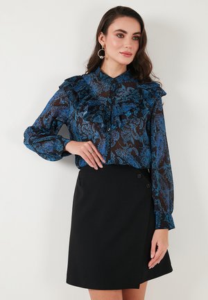 Blue patterned blouse with ruffles and buttoned cuffs, paired with a black wrap skirt featuring two buttons on the side.