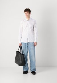 Camisa blanca de botones, jeans de pierna ancha de color azul claro, bolso de mano de cuero negro con logotipo en relieve y zapatos negros de suela gruesa.