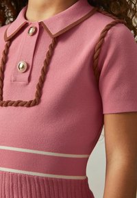 Polo stiilis kleit pehmes roosas kangas, pruuni põimitud detailide, ümmarguste kuldsete nööpide ja kreemjate horisontaalsete triipudega vööl.