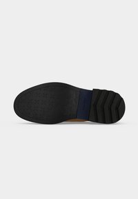 Semelle noire d’une chaussure habillée avec un motif croisé à l’avant et des rainures horizontales au talon, présentée sur fond blanc.