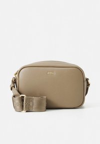 Brūna ādas taisnstūrveida plecu soma ar zelta detaļām un rakstainu siksnu ar zīmola nosaukumu. Gluda tekstūra, minimālistisks dizains.