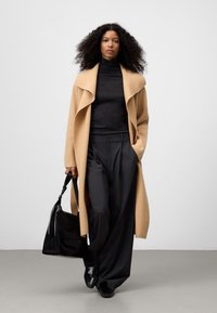 Cappotto beige lungo, dolcevita nera, pantaloni grigi a gamba larga, borsa nera. Tessuti lisci, colori neutri, vestibilità rilassata.