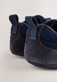 Chaussures bleu marine en daim doux et mesh, présentant des surfaces texturées et des languettes au talon pour un enfilage facile.