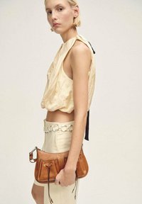 Brown leather handbag with gathered design and drawstring closure. Features silver hardware and adjustable strap. Model wears a beige top and skirt.