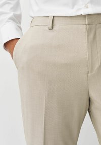 Pantalones beige ajustados, confeccionados en una tela texturada, con un corte estilizado, bolsillos laterales y un brillo sutil.