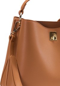 Tandfarvet læderhåndtaske med en struktureret form, udstyret med en guldfarvet lås, tekstureret overflade og to transportmuligheder: et øverste håndtag og en aftagelig rem.