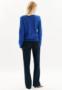 Maglione blu a maglia con maniche lunghe e scollatura rotonda, abbinato a pantaloni flared in denim scuro, visto da dietro.