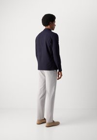 Chemise à manches longues bleu marine, pantalon gris et chaussures beige. La chemise possède un col et des boutons, tandis que le pantalon est ajusté et légèrement fuselé.