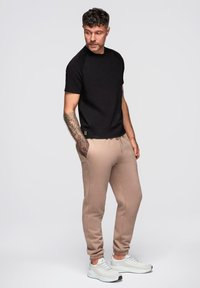 Sort kortærmet t-shirt kombineret med beige joggers, der har elastisk talje og manchetter ved anklerne. Hvide sneakers fuldender outfittet.