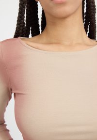 Langermet topp i beige med en gradient fra lys beige til myk rosa, med rund hals og ribbet tekstur.