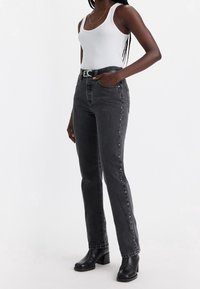 Jeans negros de talle alto con pierna recta, que cuentan con un diseño de cinco bolsillos y botones de metal. Combinados con una camiseta sin mangas blanca y botines negros.