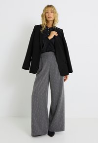 Pantalones anchos gris con un sutil patrón vertical, combinados con una chaqueta negra. La tela muestra una textura suave y un diseño estructurado.