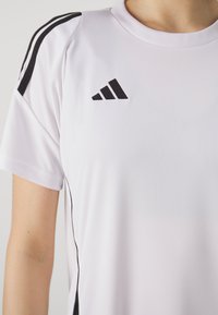 Witte sport t-shirt met zwarte zijstrepen en een geborduurd zwart logo op de borst. Gemaakt van lichtgewicht, gladde stof.