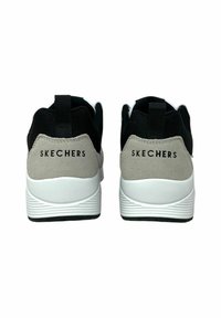 Baskets Skechers noires et grises avec un dessus en mesh rembourré, semelle en caoutchouc blanc et logo signature à l'arrière. Accents texturés à l'arrière.
