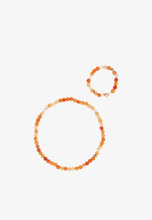 Twee kralenarmbanden gemaakt van ronde oranje en crèmekleurige kralen, één groter en één kleiner, op een witte achtergrond.