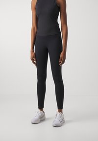 Svart sömlös träningsöverdel med hög halsringning, matchad med eleganta svarta leggings. Fötter i vita sportskor med grå accenter och snören.