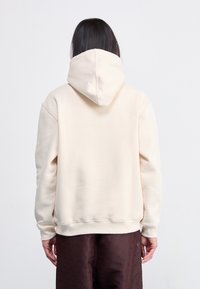 Sweatshirt creme com um capuz grande e estruturado, punhos canelados e um corte descontraído, combinado com calças castanhas com padrão.