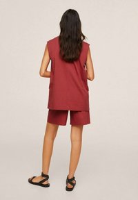 Haut sans manches marron et short assorti. Le tissu semble lisse. Porté avec des sandales noires. Vue de dos montrant les cheveux qui tombent en cascade.