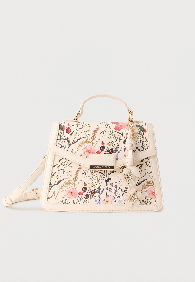Sac à main crème avec imprimé floral, poignée supérieure, bandoulière amovible et breloques en forme de fleurs suspendues sur le rabat avant.