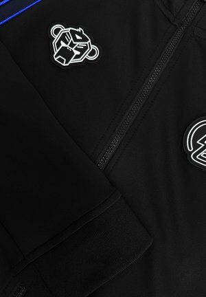 Zwarte zip-up jas met ribgebreide manchetten, voorzien van twee zwart-witte gestileerde dierenpatches nabij de rits.
