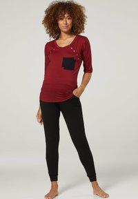 Burgundy long-sleeve top with a black pocket, button details, paired with black fitted pants. Smooth fabric, casual design, and slim shape.