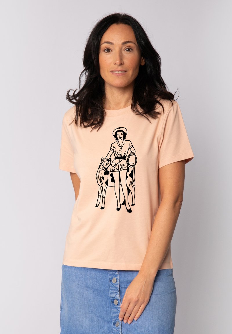 T-shirt en coton pêche avec un graphique noir représentant une figure avec deux vaches. Manches courtes et col rond. Style simple et décontracté.