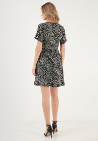 Black and beige leopard print dress with short sleeves, fitted waist, and flared skirt. Styled with black high-heeled sandals.