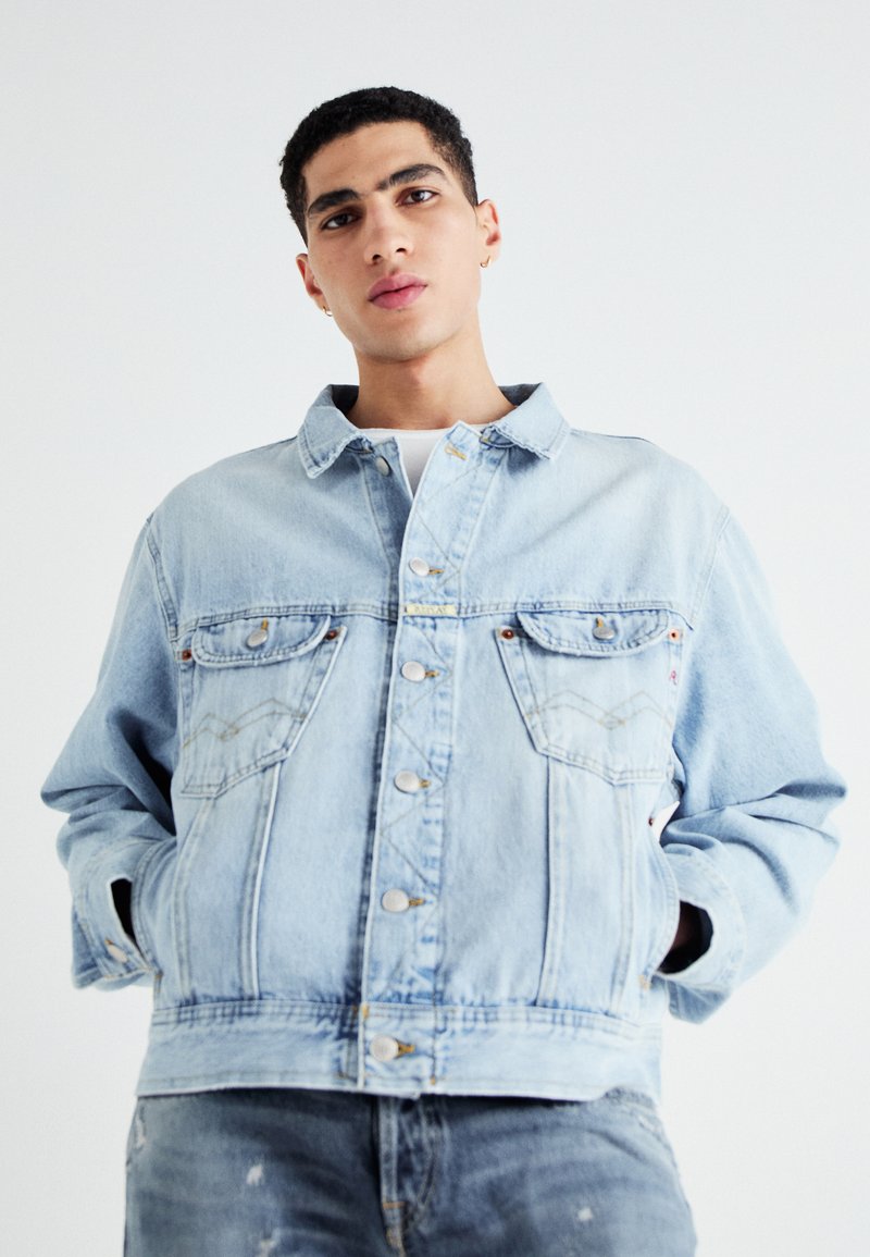 Chaqueta de mezclilla azul claro con un diseño clásico de botones, bolsillos en el pecho y un ajuste relajado con detalles de costura visibles.