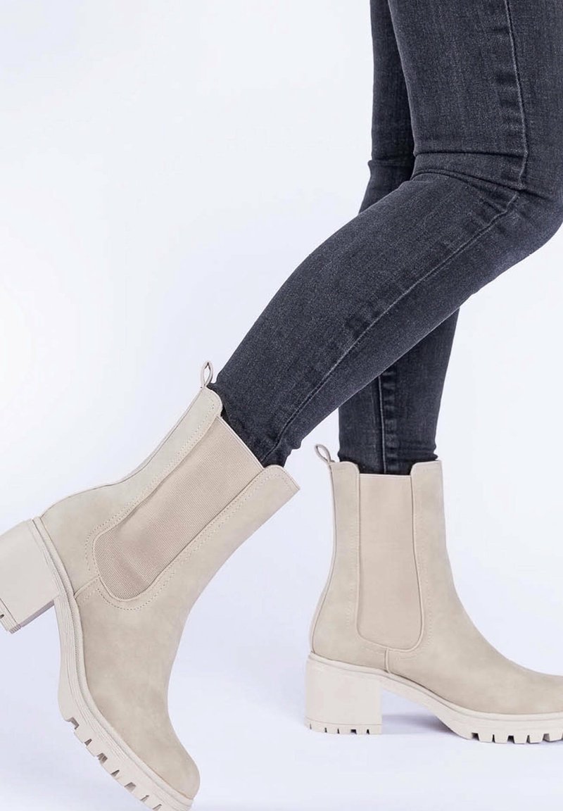Bottines beiges avec une finition en suede, des panneaux latéraux élastiques et un talon épais. Semelle texturée avec des rainures pour une meilleure adhérence.