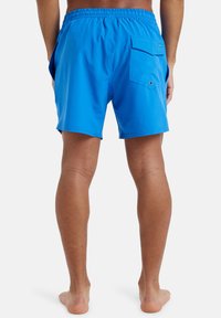 Modré plavecké šortky vyrobené z ľahkého materiálu, s elastickým pásom, bočnými vreckami a klopovým vreckom na pravom zadnom diele.