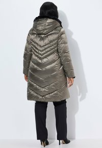 Olivengrøn pufferjakke med chevron-syninger, hætte foret med sort faux fur, knælængde, parret med sorte bukser og hæle.