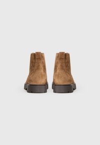 Botas de tobillo de ante marrón con una superficie texturizada, tiradores en el talón y suelas de goma oscura y resistente para mayor tracción.