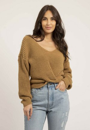 Pull en tricot marron chaud, avec un col en V, des manches amples et un ourlet noué. Associé à un jean déchiré bleu clair.