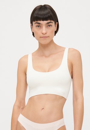 White seamless crop top with wide straps, square neckline, and a smooth, stretchy texture. Worn with light pink underwear.