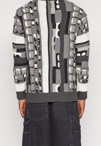 Gebreide trui met abstracte grijze en witte patronen, met textuurrijke strepen en geribbelde boorden. Materiaal is zacht en lichtgewicht.