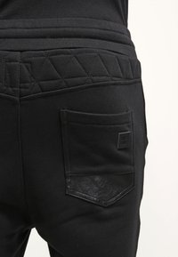 Černé tepláky s prošívaným pasem, se zadní kapsou z kůže a hladkým pleteným textilním povrchem.